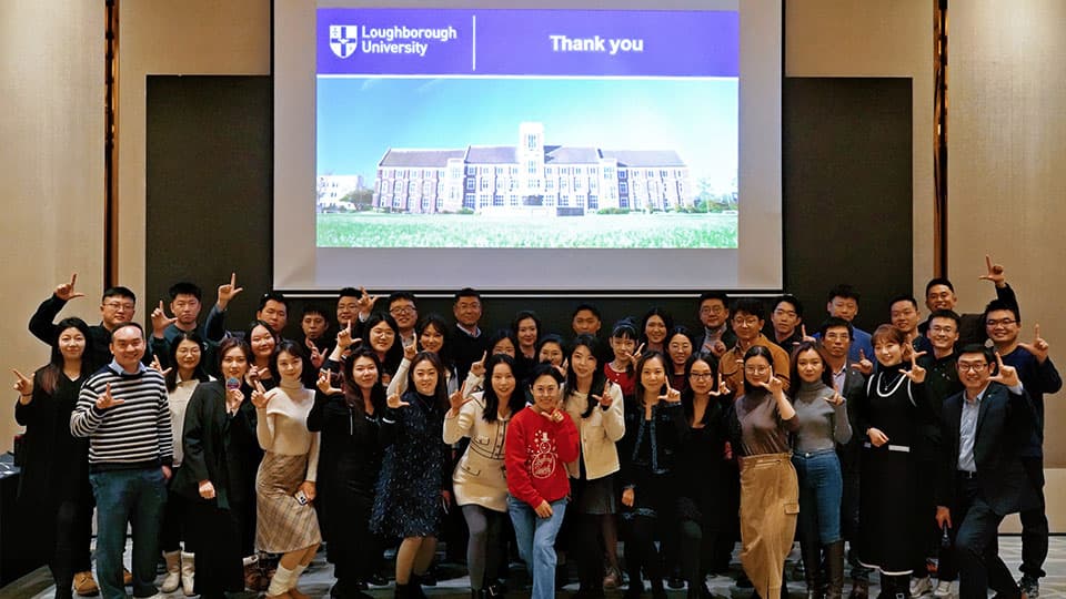 A group of alumni at an end-of-year event in front of a presentation with the Loughborough University logo on it in Beijing.